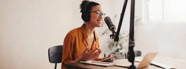 Woman recording a podcast on her laptop computer with headphones and a microscope. Female podcaster making audio podcast from her home studio.