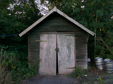 Old wooden hut with ill fitting door with two silver barrels beside