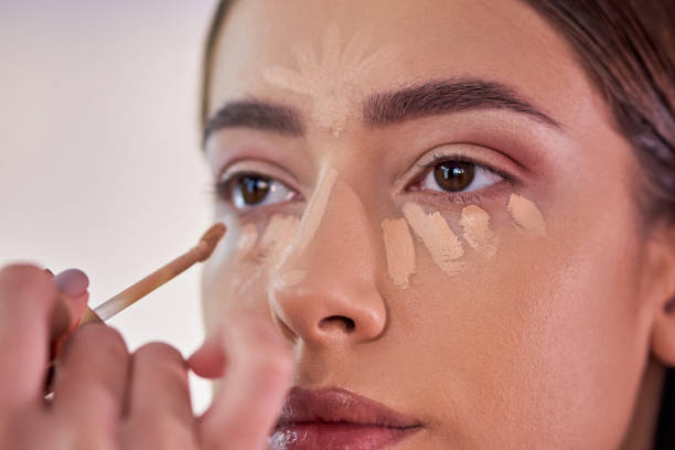 Make up artist applying a concealer under eye area, to hide dark eye circle Dedicated young female make up artist applying a concealer under customer's eye to hide skin irregularities, while giving her professional service at her make up studio Foundation and Concealer stock pictures, royalty-free photos & images