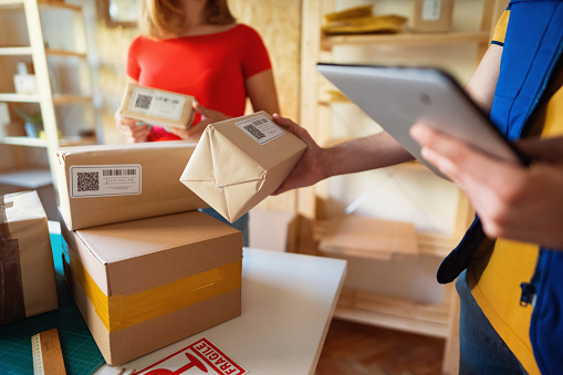 Close view of the delivery man holding and checking package details while unrecognizable young women holding package in the office.