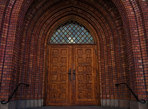 Closed wooden church door in a red brick arch entrance.