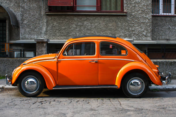 orange vintage volkswagen beetle car on a street in bucharest. - beetle imagens e fotografias de stock