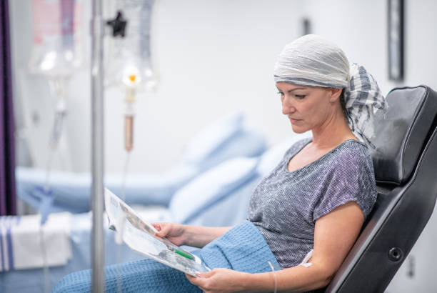 Oncology patient in the hospital A woman wearing a head scarf sits on a hospital chair with a blanket over her lap. She is hooked up to an IV, and resting and reading a magazine. chemotherapy drug stock pictures, royalty-free photos & images