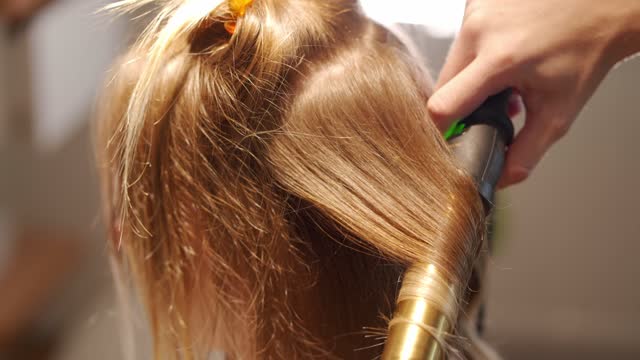 Hairdresser using an iron hair curler to make a modern wavy hair style