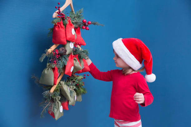 una niña con sombrero de navidad y pijama en busca de dulces y regalos en el calendario de adviento. - advent calendar advent christmas childhood fotografías e imágenes de stock