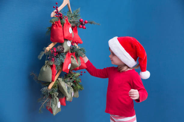 a child girl in a christmas hat and pajamas searching for candy and gifts in advent calendar. - advent calendar advent christmas childhood imagens e fotografias de stock