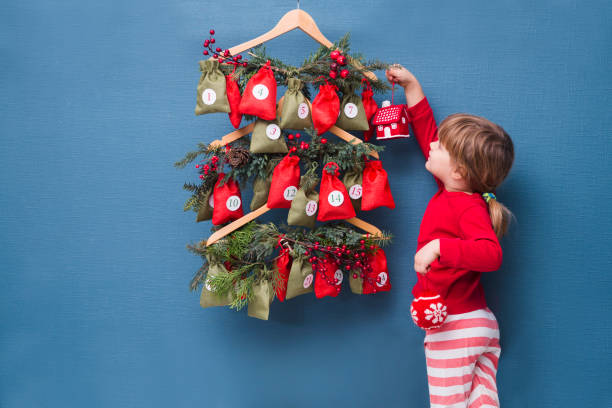 una niña con sombrero de navidad y pijama en busca de dulces y regalos en el calendario de adviento. - advent calendar advent christmas childhood fotografías e imágenes de stock