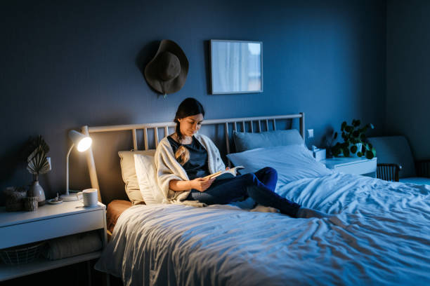Woman reading a book at night Young woman lying on the bed and reading a book at night. The room is dark and blue and the light on the night stand is illuminating the book. Bedroom, horizontal photo bed stock pictures, royalty-free photos & images
