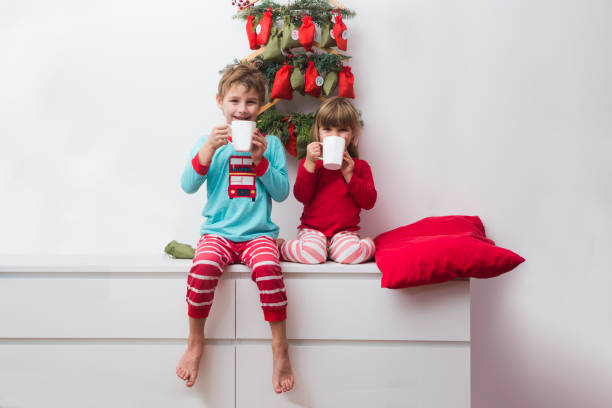 dos niños hermano y hermana en pijama bebiendo cacao con dulces del calendario de adviento en casa. hygge. feliz familia en vacaciones de navidad. - advent calendar advent christmas childhood fotografías e imágenes de stock