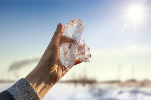 Ice in a man's hand against the backdrop of the bright sun. Global warming concept. Seasonal weather. End of winter. Spring.