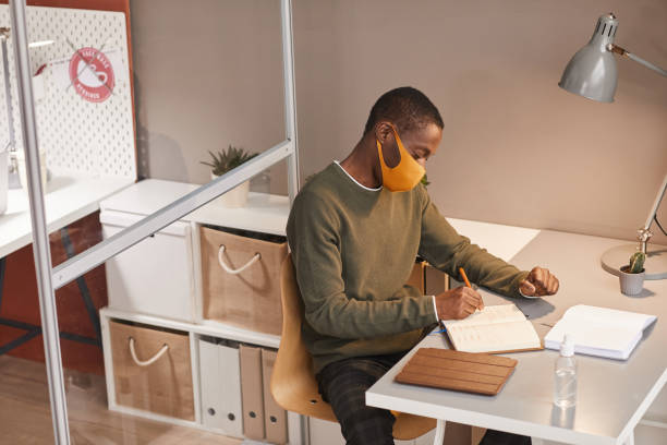 istock Young African Man Wearing Mask at Desk 1287472361