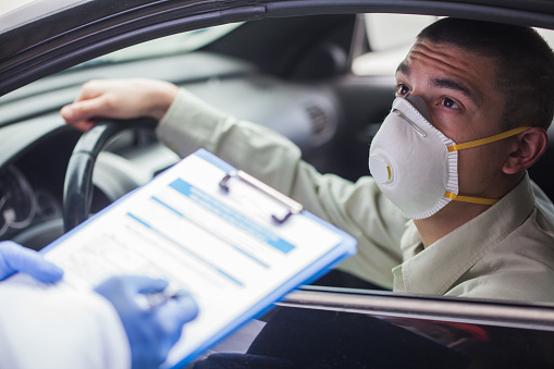 Young man wearing protective face mask in drive-thru Coronavirus car testing center, answering health check questionnaire, doctor or paramedic performing US point of care COVID19 test, rt-PCR diagnostic