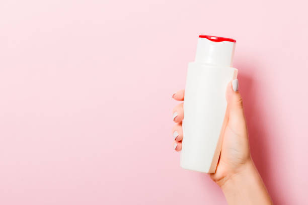 Woman's hand is holding a cosmetics bottle at pink background with copy space for your design