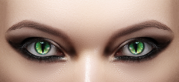 Close-up of Woman Eyes. Halloween Makeup. Cat Eye Lens. Fashion Catwalk Black Make-Up. Luminous Green Cats Eyes. Close up Shot