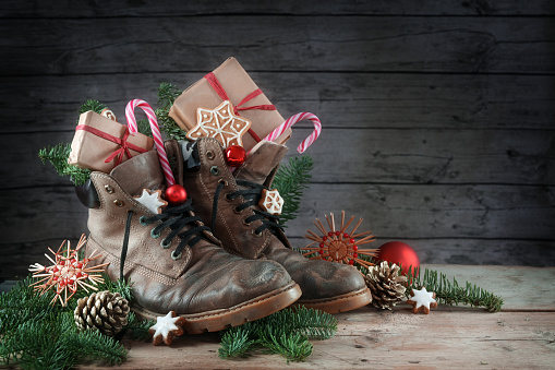 Botas de senderismo viejas llenas de dulces, regalos y decoración de Navidad en el día de Nicholas, o etiqueta alemana Nikolaus, el 6 de diciembre es tradición poner los zapatos al aire libre, fondo rústico de madera con espacio de copia photo