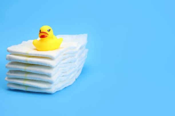 istock Baby disposable diapers on a blue background in a stack and a rubber duckling, copy space for text 1287476983