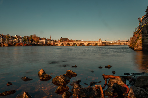 Low angle view over the water with the historical skyline of Maastricht with the old bridge connecting two parts of town crossing the river Meuse.