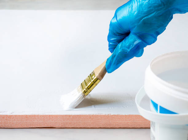 istock gloved hand holds brush and paints white surface 1287480734