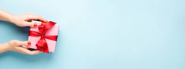 istock Female hands holding gift box on blue background. 1287483955