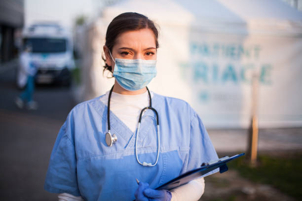 Coronavirus medical worker Portrait of very tired & exhausted UK NHS ICU doctor in front of hospital, emergency patient triage tent in background,Coronavirus COVID-19 pandemic outbreak crisis, medical staff working long shifts muster station stock pictures, royalty-free photos & images