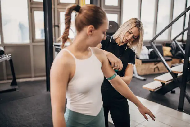Photo of Young female personal trainer measuring woman's arms at the gym