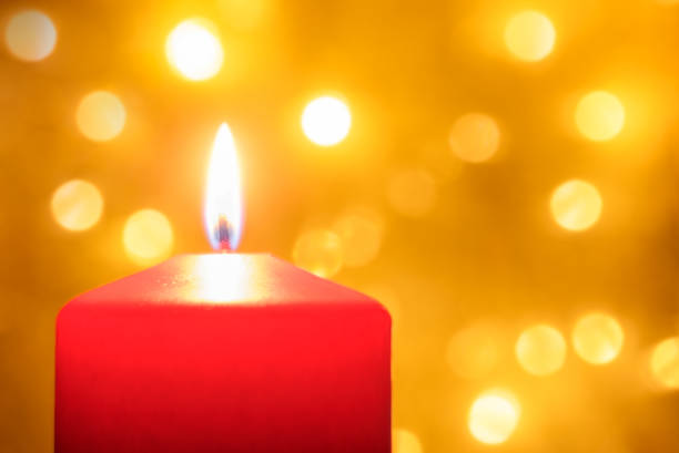 Close up of a burning red Christmas candle with defocused lights in background. Bokeh effect and copy space.