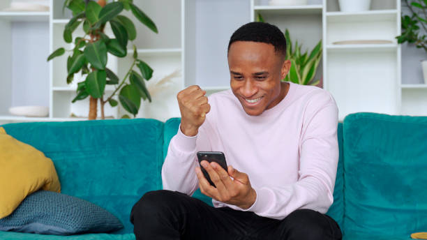 istock Black man winner holding smartphone feeling euphoric with mobile online bet bid game win 1287492790