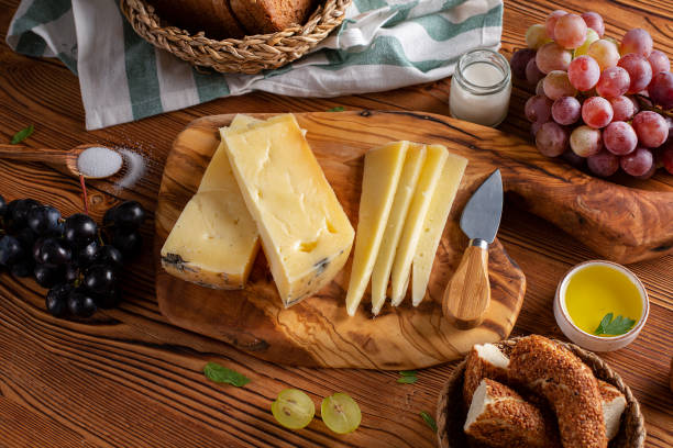 Gruyere cheese on wooden table with wooden cutting board, knife and props stock photo