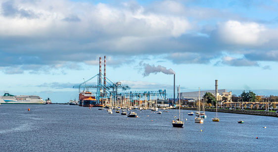 A view of Dublin Port, Ireland, with a gantry crane in operation, a passenger ferry berthed,  small boats and the East Link Ferry Bridge and the new incinerator in the distance.