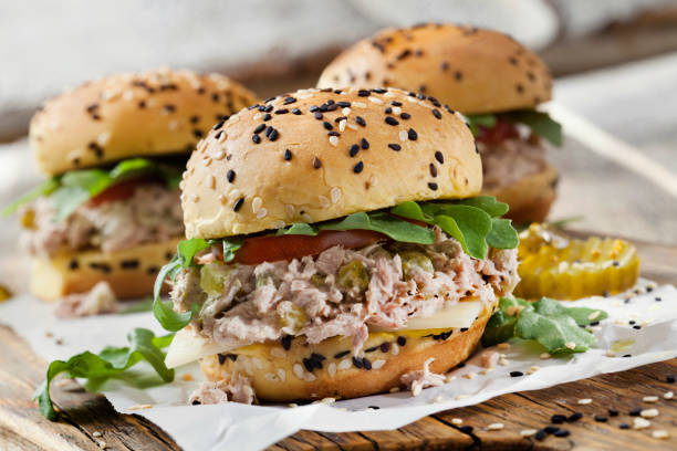 cursori di insalata di tonno cremoso con sottaceti dolci, formaggio svizzero, pomodoro e rucola su panini di semi di sesamo brioche - burger bun sandwich bread foto e immagini stock