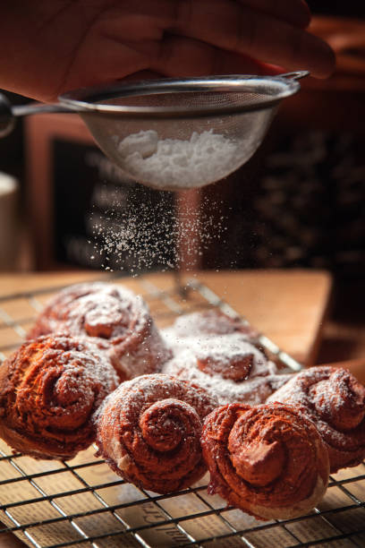 Close Up view chef sprinkle icing sugar over the cinnamon rolls