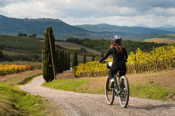 Bike excursion on country road in Val d'Orcia with electric Mountain bike - Tuscany, Italy Young cyclist riding her electric mountain bike during an excursion on country road in Val d'Orcia - Tuscany, Italy. biker photos stock pictures, royalty-free photos & images