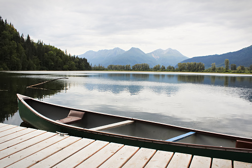 Side view of canoe tied to a dock with mountains in the background.