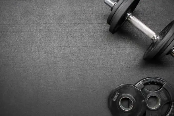 Barbell and dumbbells on the floor at the gym. Top down view flat lay with bodybuilding equipment on a black background and empty space for text. Fitness, weight training or healthy lifestyle concept