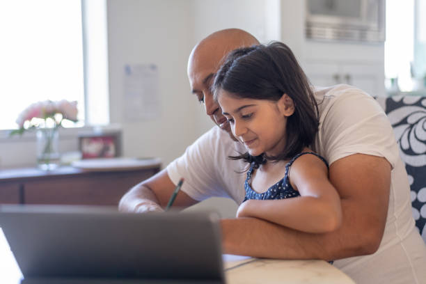 istock Father helping elementary age daughter with e-learning video conference call and online school assignment 1287510109