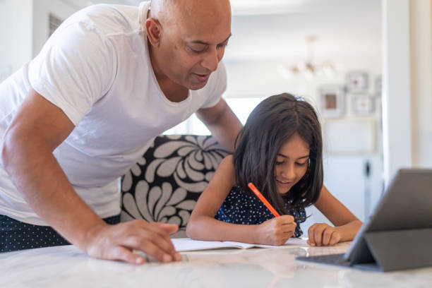 istock Father helping elementary age daughter with e-learning video conference call and online school assignment 1287510110
