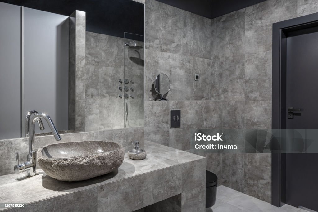 Dark and modern bathroom Dark and modern bathroom with gray wall tiles, stone like washbasin and big mirror Bathroom Stock Photo