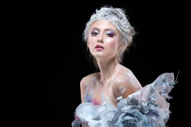 Photo of Winter Beauty Woman in clothes made of frozen flowers covered with frost, with snow on her face and shoulders. Christmas Girl Makeup. Make-up the snow Queen. Isolated on a black background