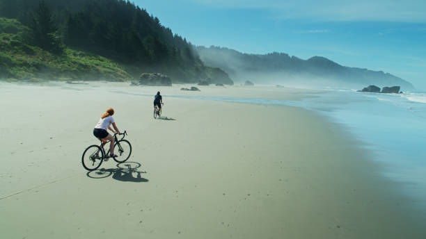 plage d’équitation d’homme et de femme sur le sable humide de la plage de whaleshead dans l’oregon - oregon beach photos et images de collection