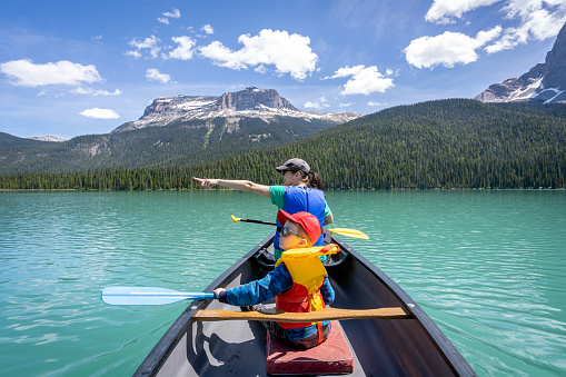 POV Family canoeing at Emerald Lake in Summer, Yoho National Park, British Columbia, Canada. The mother and her son are looking at the beautiful view and the mother is pointing out something to her son.