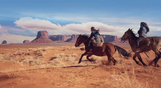 Navajo siblings riding fast on horses in Monument Valley Arizona - USA Navajo siblings riding fast on horses in Monument Valley Arizona - USA monument valley tribal park photos stock pictures, royalty-free photos & images