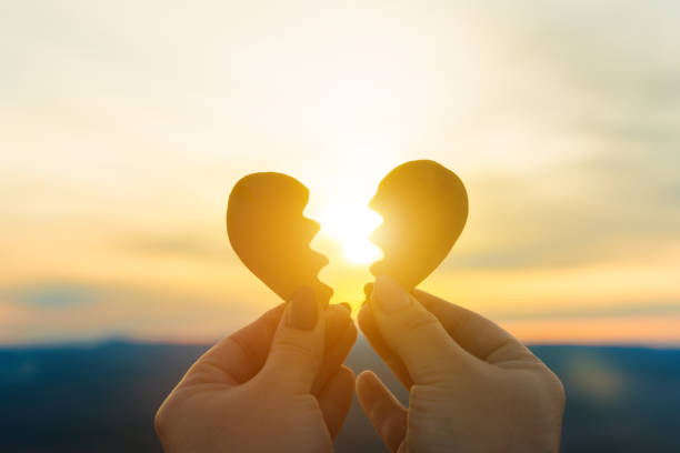 istock Two hands hold a broken heart on the background of the sunset. 1287532511