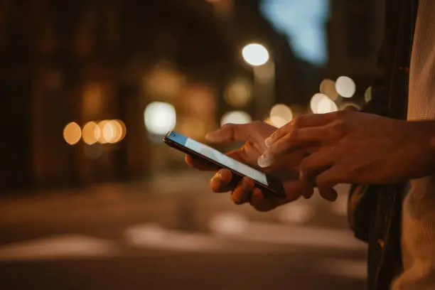 Photo of Male hands with smartphone. Night street on background. Man with mobile phone outdoors.