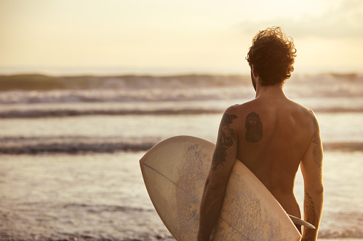 Athletic man surfer stands with blank white surfboard at sunset ocean beach