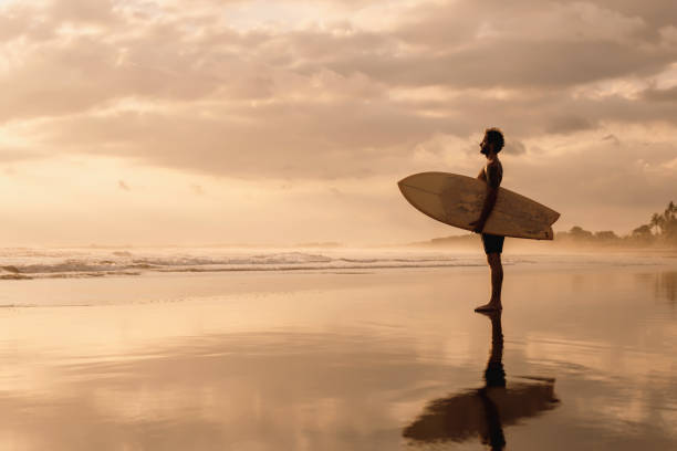 istock Surfer stands on sunset ocean beach 1287538851