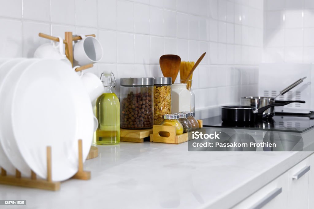 Untensil on counter in kithcen. Modern white counter in kitchen with dishes, utensil, cereal, seasoning in container and stove. Cup Stock Photo