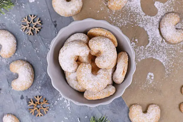 Top view of crescent shaped christmas cookies called 'Vanillekipferl', a traditional Austrian or German Christmas biscuits with nuts and icing sugar surrounded by Christmas decoration in bowl