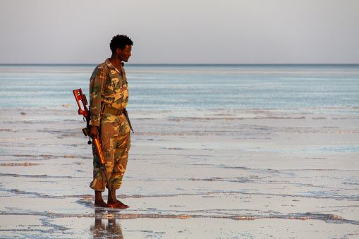Lake Karum, Ethiopia - Jan 16, 2014: Ethiopian National Defense Force (ENDF) soldiers escort foreigners near the border with Eritrea. The soldier standing in the salt lake with a Dragunov sniper rifle in his hand.