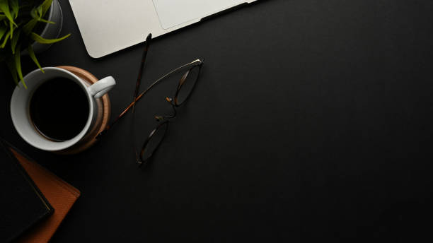 istock Black table with copy space, eyeglasses, supplies and coffee cup in home office room 1287547515
