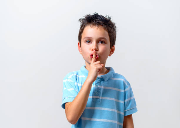 istock A boy in a blue T-shirt calls for a gesture to shut up. Keep quiet. 1287547803